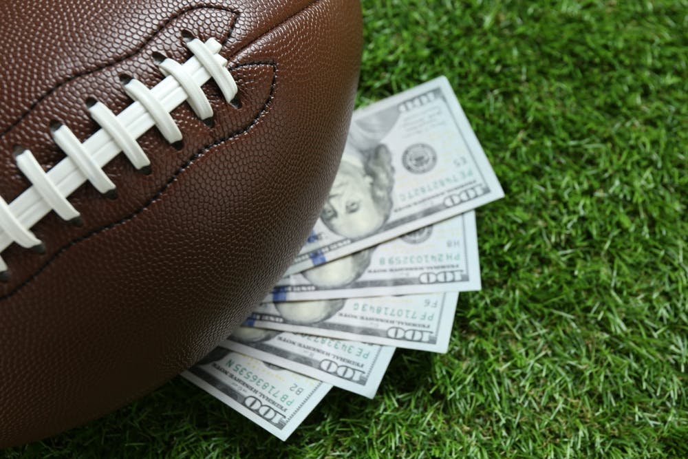 Football sitting on top of money on grass.