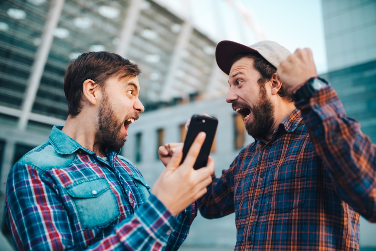 Two men excited about sports betting outside of a sports stadium. 