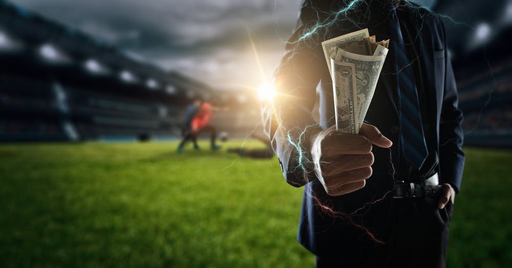 Man holding money to bet on a soccer game going on in the background. 