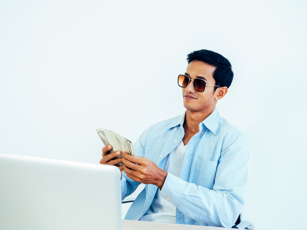 Man holding cash in front of a computer for sports betting. 