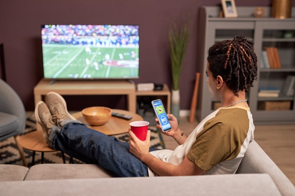 Someone sports betting on a football game and watching the game.