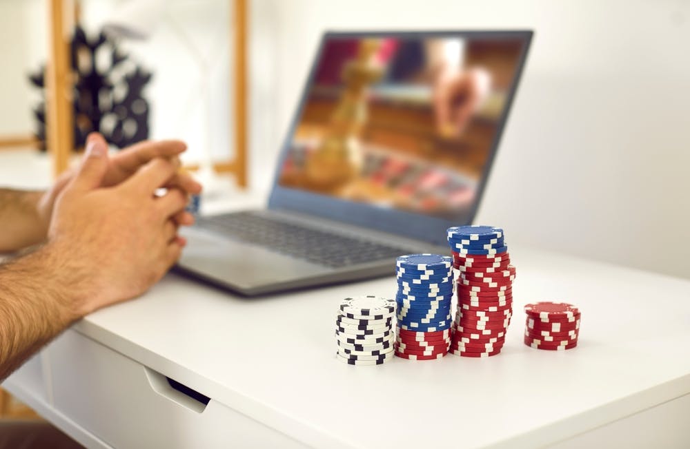 An individual playing online casino games with poker chips next to the computer. 