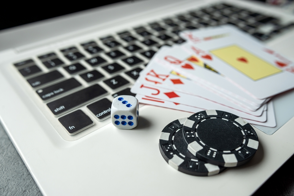 Laptop keyboard with dice, poker chips and playing cards sitting on it. 