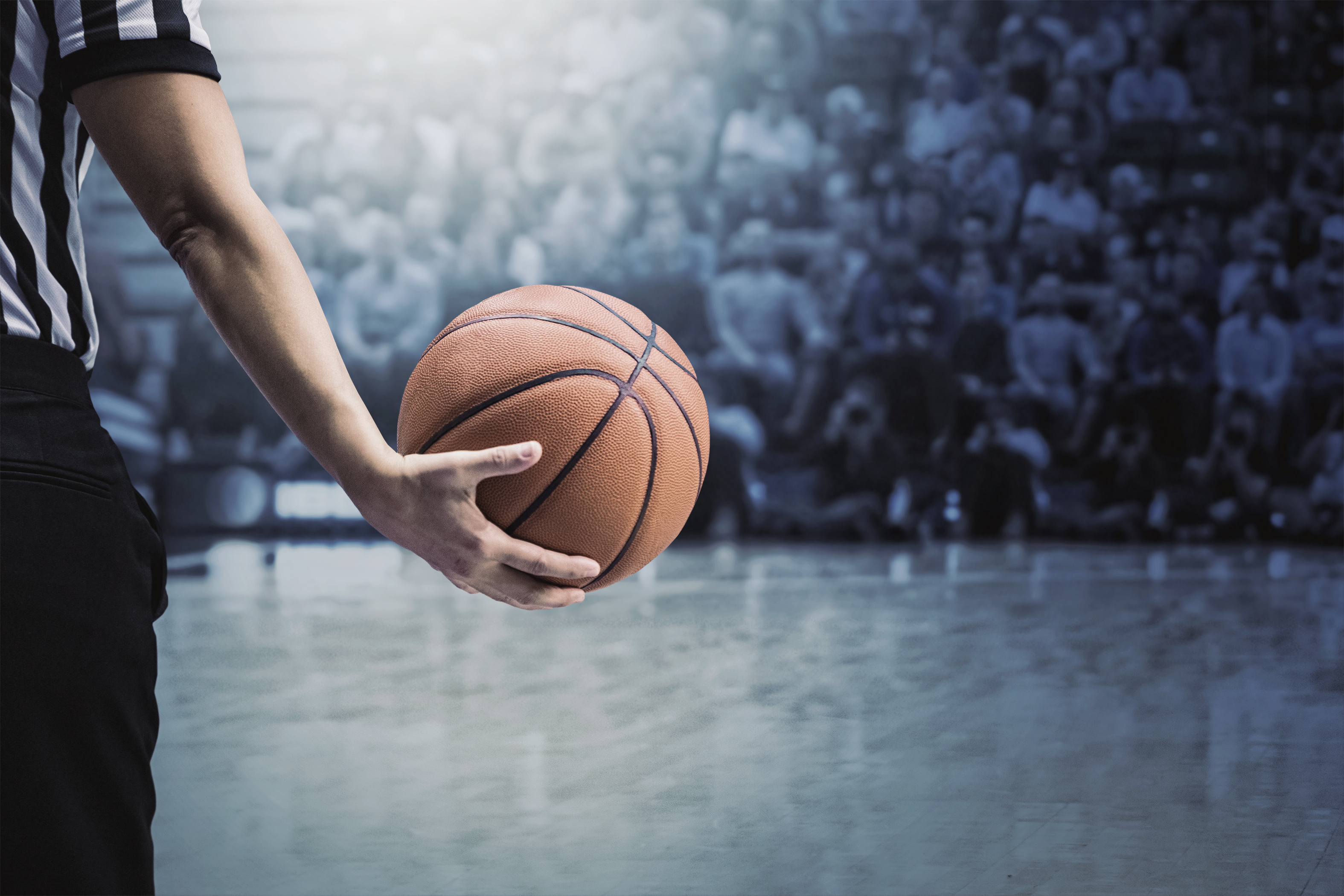 Basketball referee holding a basketball at a game in a crowded sports arena. 